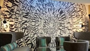 Quarto com um mural circular na parede, duas poltronas, uma mesa pequena e um tapete estampado.