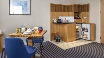 A compact hotel room with a kitchenette, a dining area with a table and chairs, and a small refrigerator.