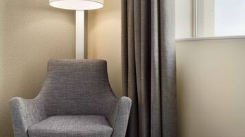A chair with a textured fabric, a lamp with a white shade, and a window with curtains.