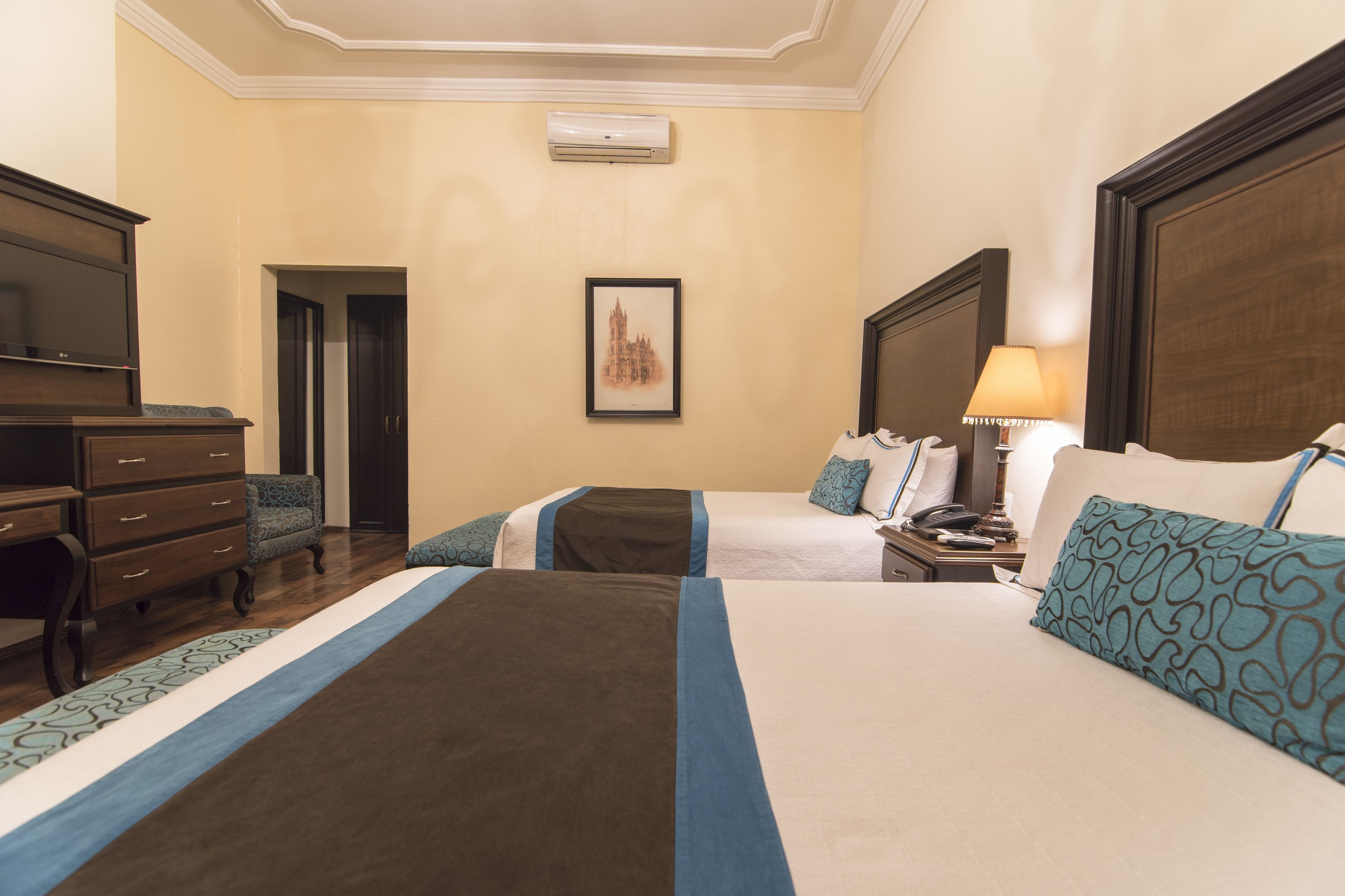Quarto de hotel com duas camas, um penteadeira, uma televisão e um quadro na parede.
