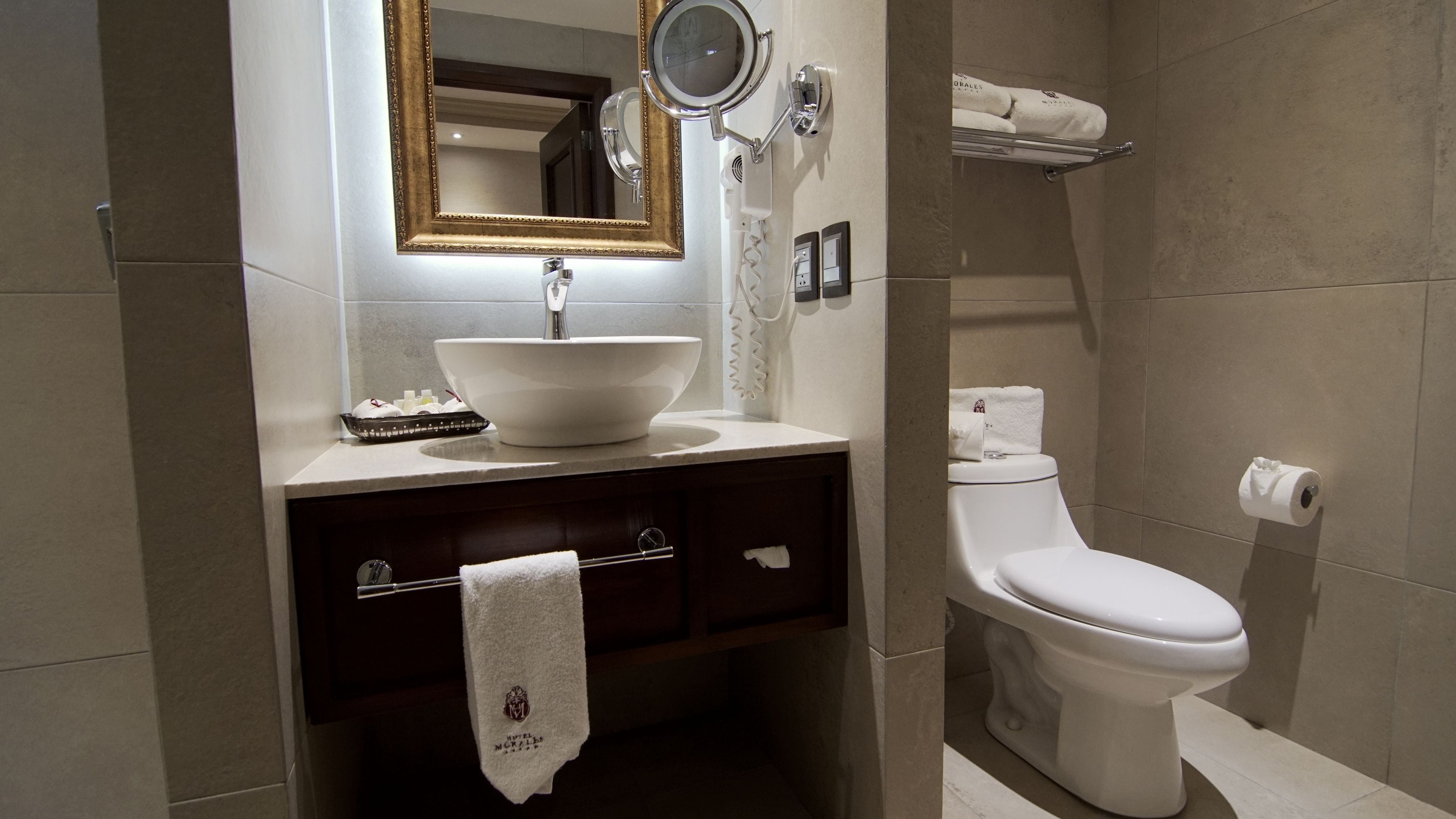 A modern bathroom with a white sink, a large mirror, a toilet, and a towel rack.