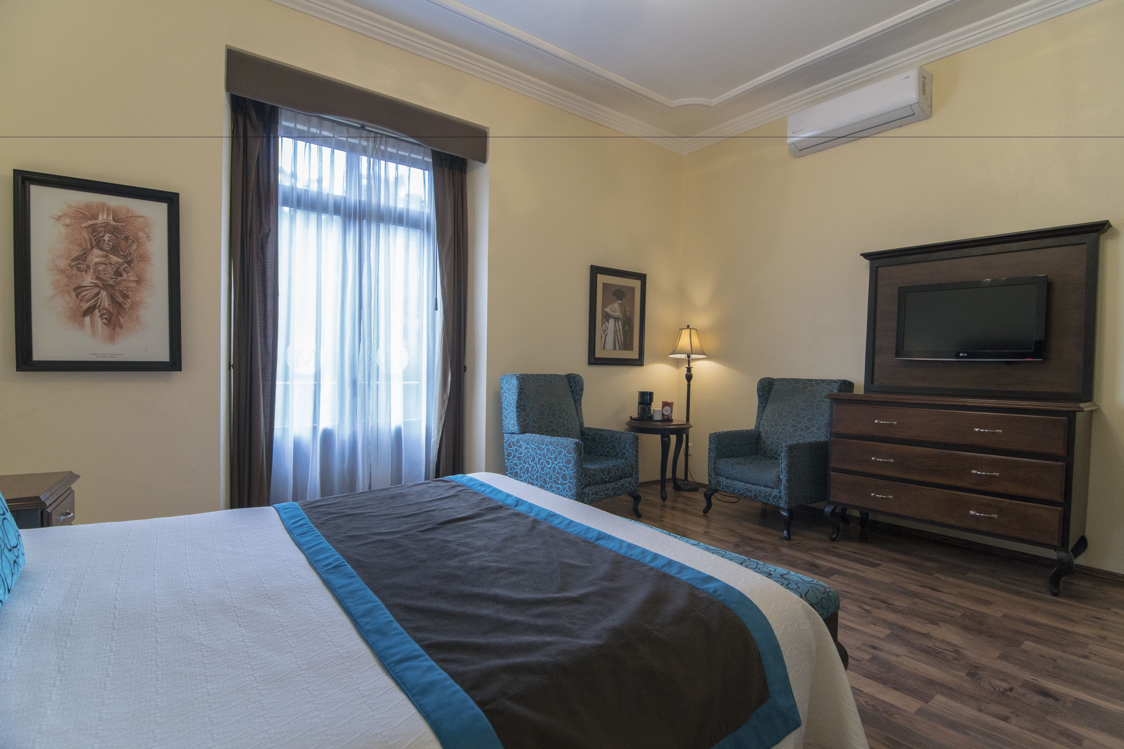 Hotellihuone, jossa on suuri sänky, kaksi tuolia, televisio ja lipasto.