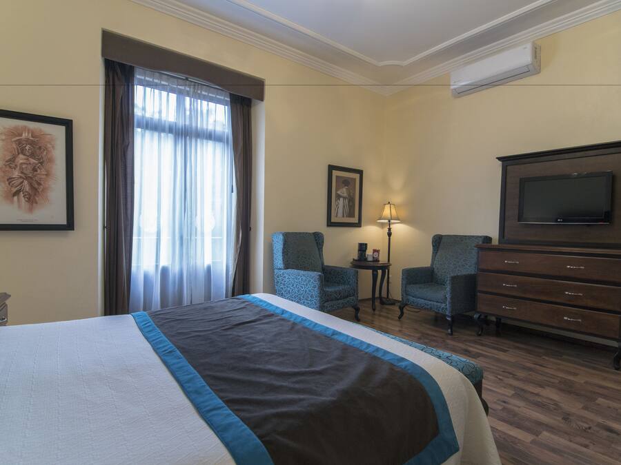 Hotellihuone, jossa on suuri sänky, kaksi tuolia, televisio ja lipasto.