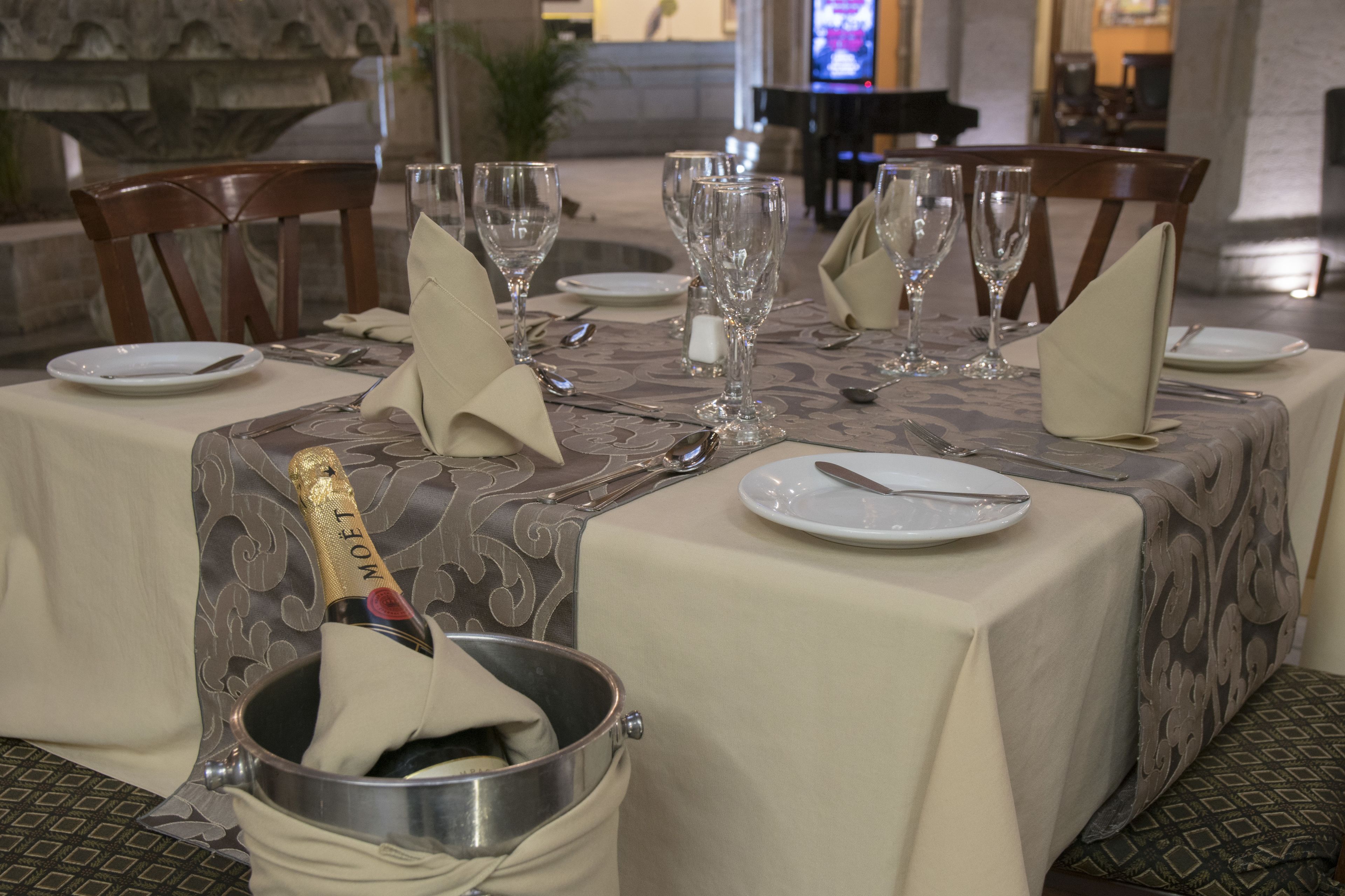 Una mesa de comedor dispuesta con platos blancos, cubiertos y copas de vino, con una botella de champán en un cubo.