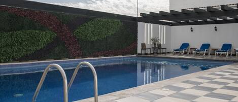 Una piscina con suelo a cuadros, sillas de descanso y una pared con jardín vertical.