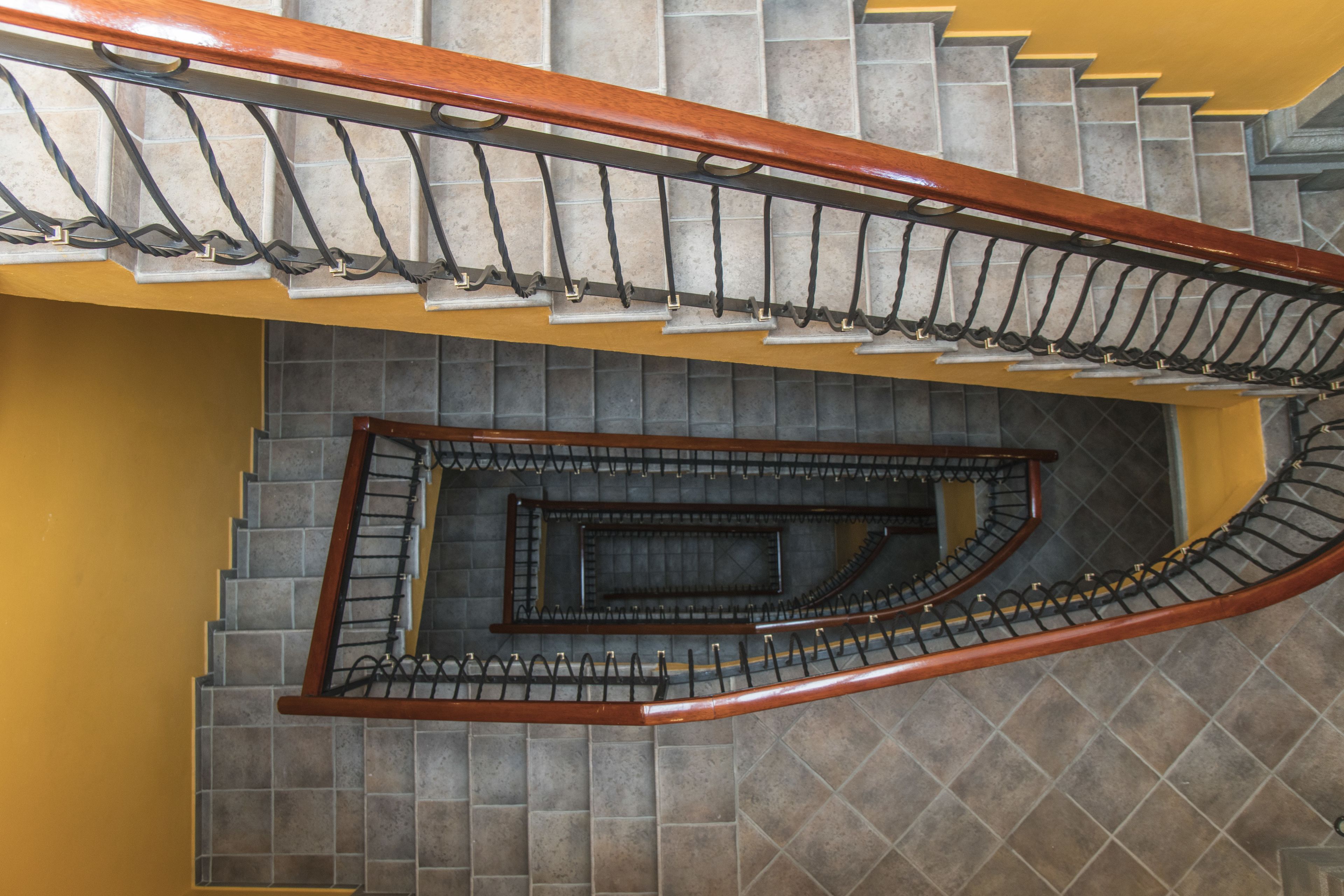 A spiral staircase with a wooden handrail and metal balusters, leading to a lower level.