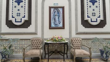 A room with two chairs, a table with a floral arrangement, and a framed religious painting on the wall.