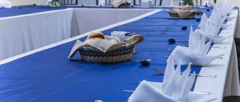 A long table with blue tablecloths, white napkins, and baskets of bread.