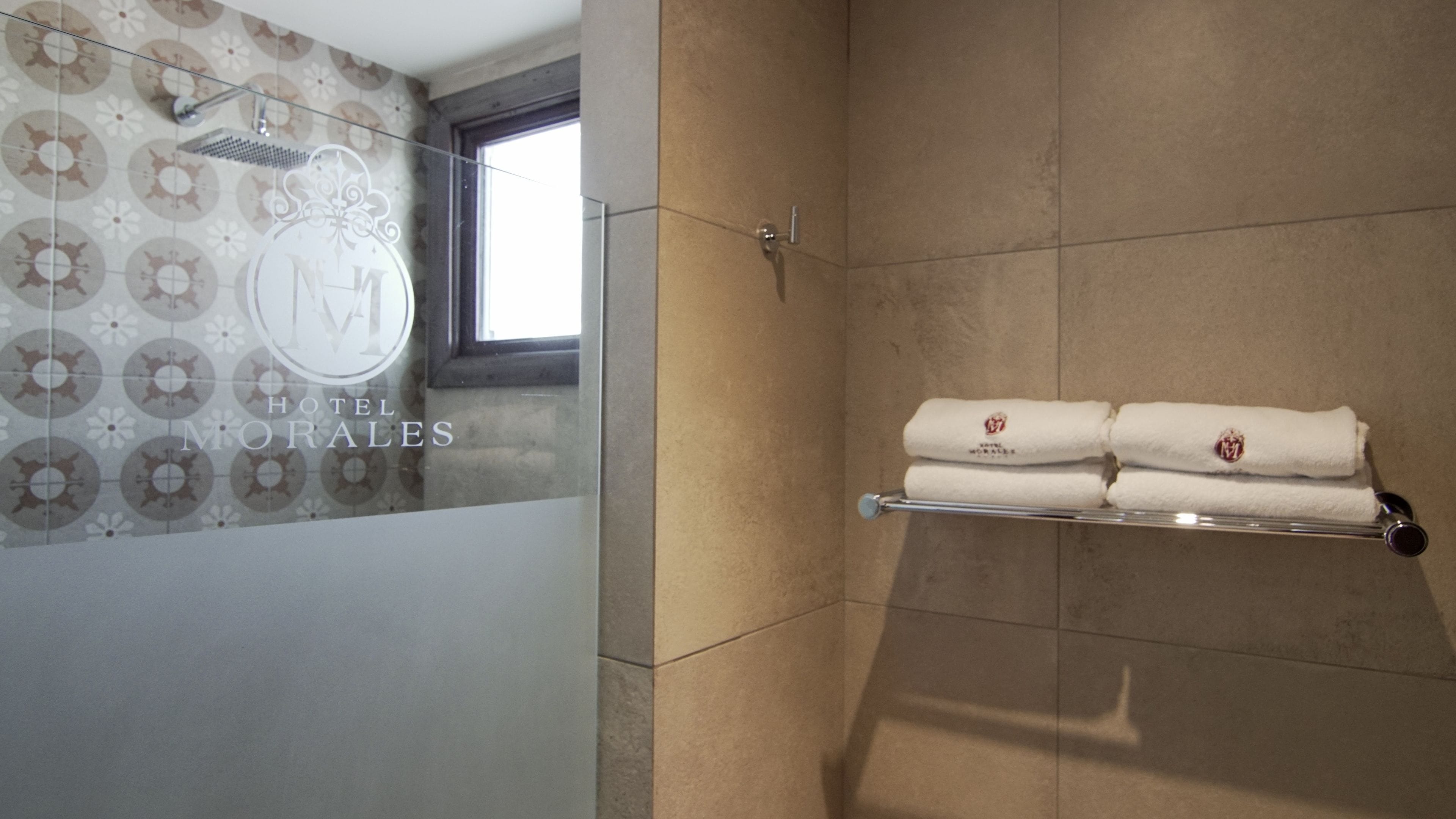 Une salle de bain d’hôtel avec une douche, un porte-serviettes avec des serviettes et un mur décoré d’un motif.