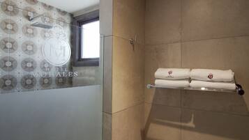 A hotel bathroom with a shower, a towel rack with towels, and a patterned wall.