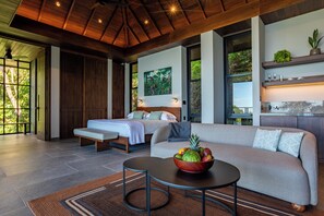 A modern bedroom with a bed, a sofa, and a dining area with a fruit bowl.