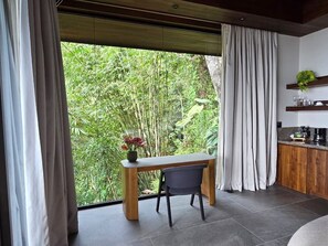 A modern room with a large window, a wooden table, a chair, and a kitchen area with a countertop and cabinets.