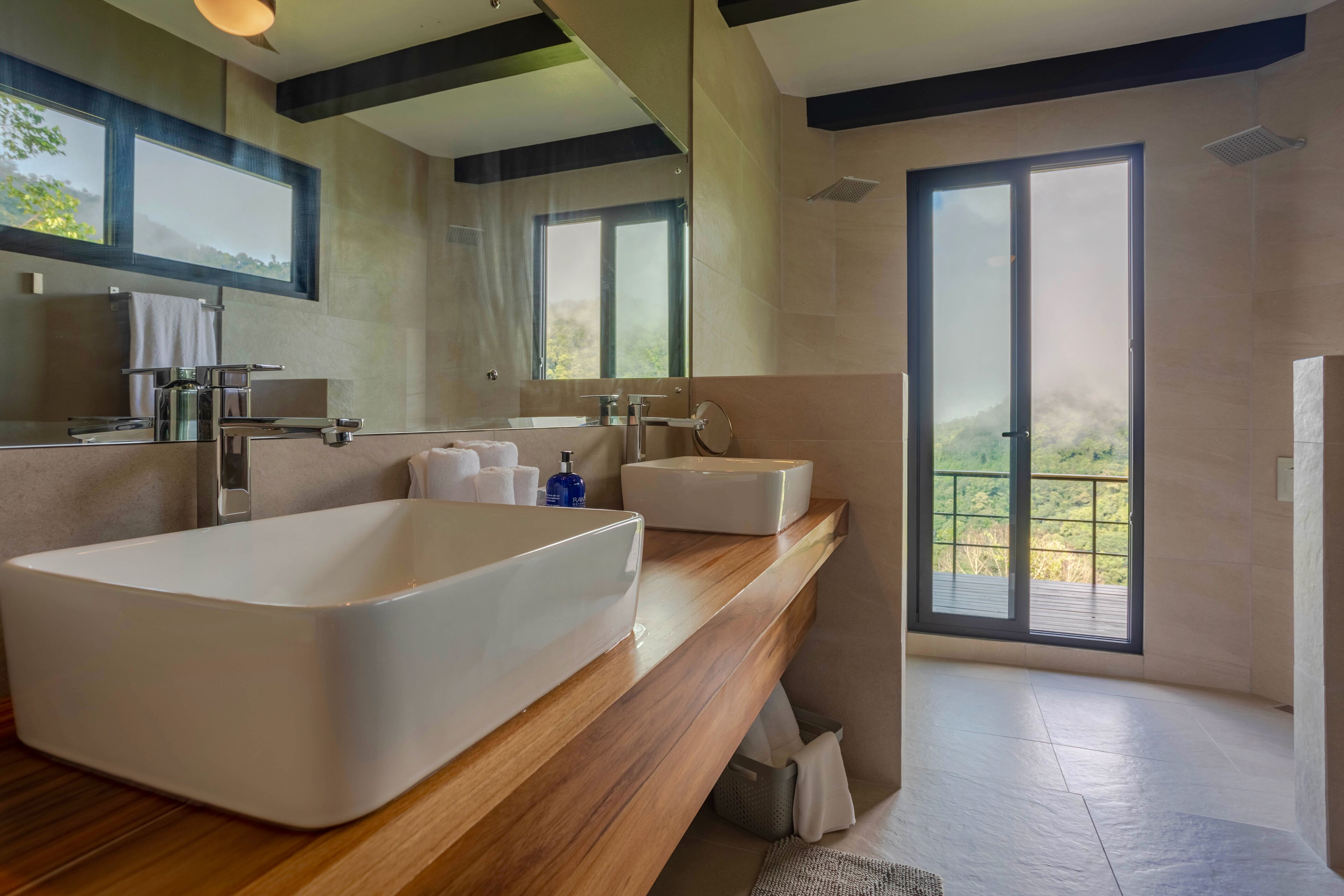 A modern bathroom with a large bathtub, a wooden vanity, and a large window offering a view of the outdoors.