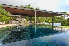 A modern outdoor pool area with a covered seating area and a bar.