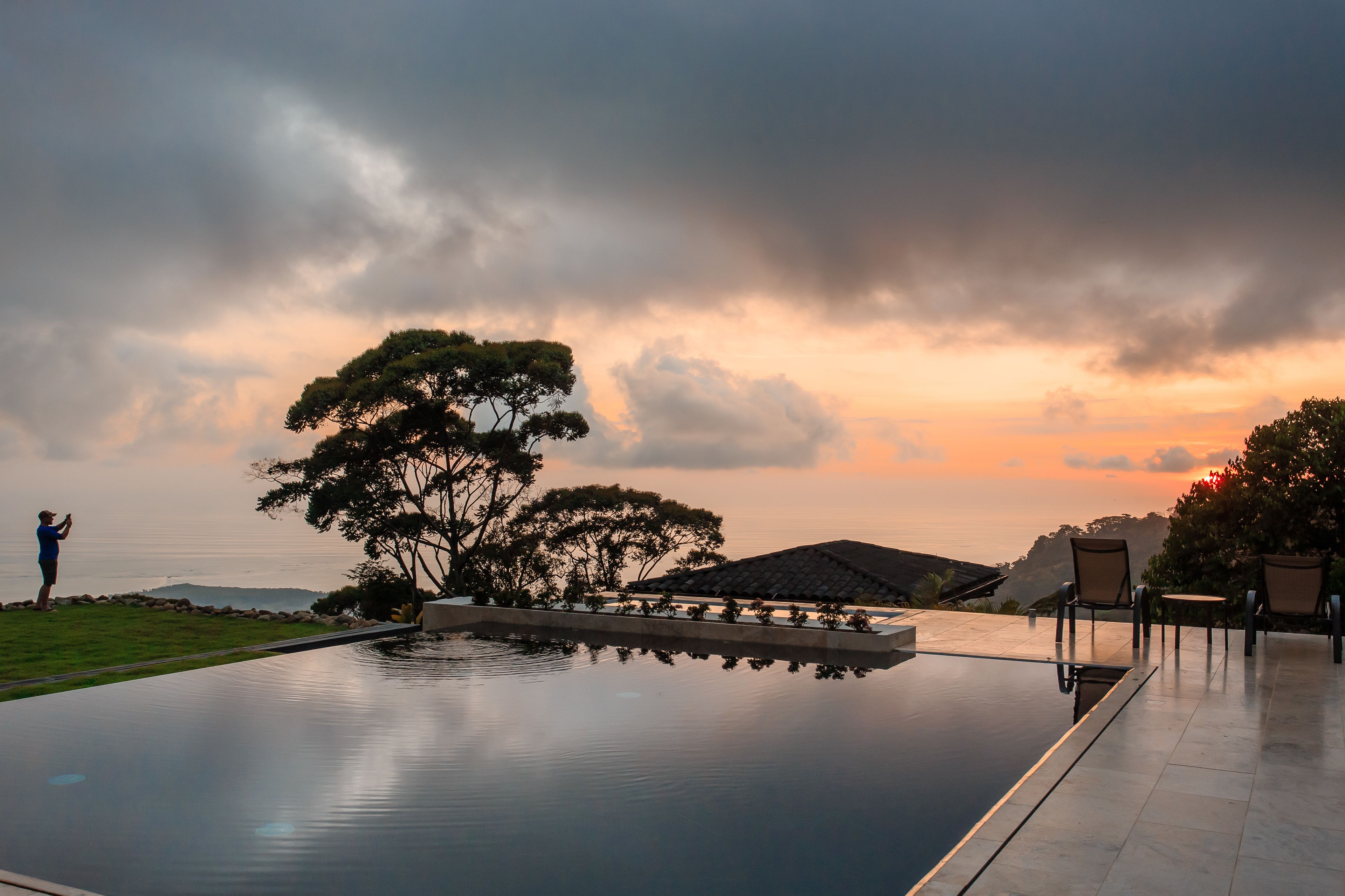 Ein ruhiger Infinity-Pool, der den Himmel spiegelt, umgeben von einer gepflegten Rasenfläche und einigen Stühlen.