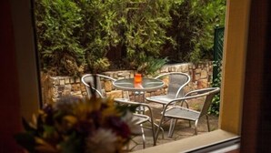 A patio with a round table and chairs, a vase with flowers, and a view of a stone wall and greenery. - Deja Vu Pension (Cluj-Napoca)