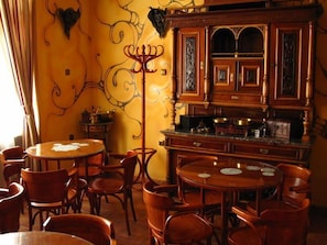 A dining area with round wooden tables and chairs, a central decorative metal stand, and a wooden cabinet with intricate carvings.