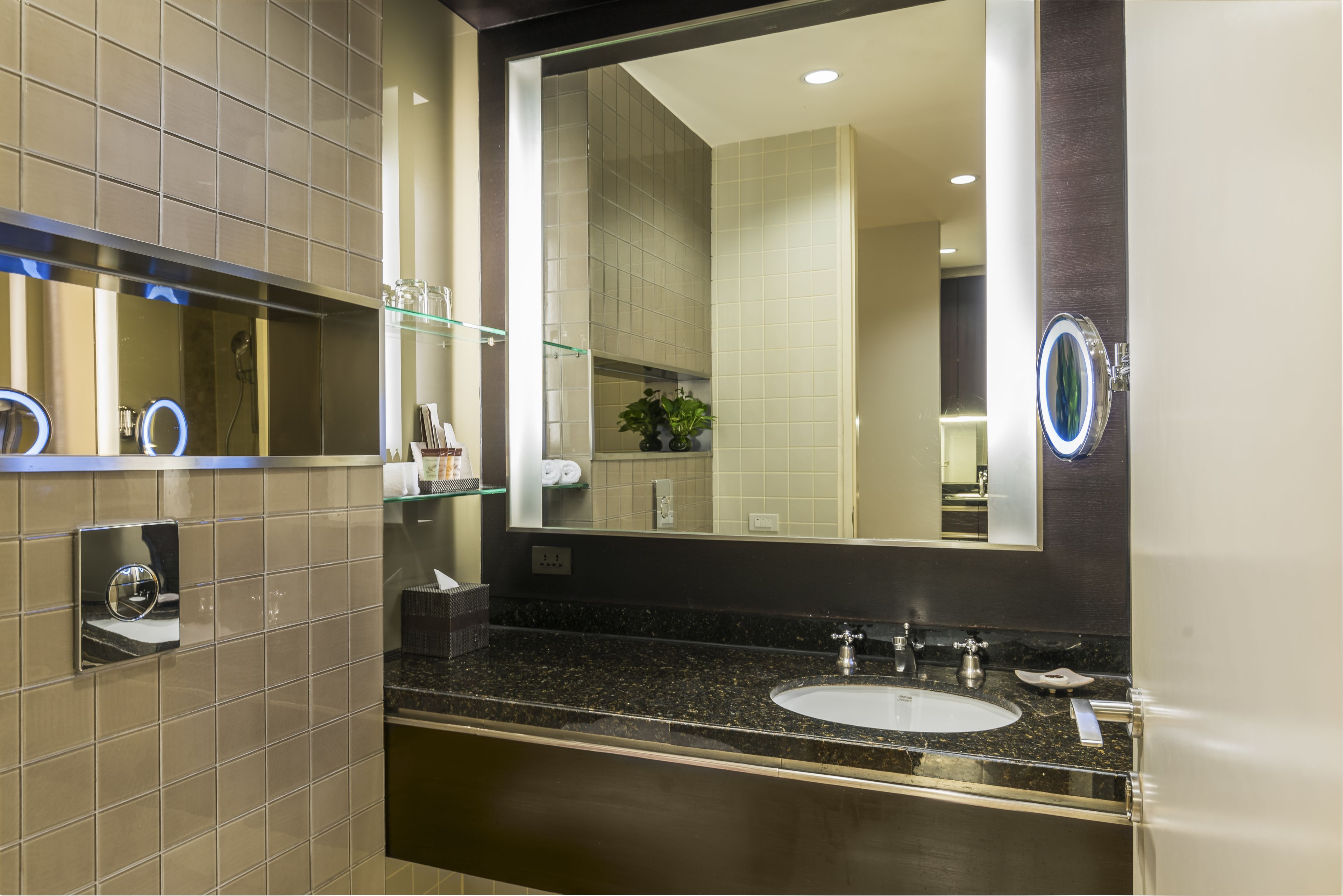 Un baño moderno con un espejo grande, un lavamanos y un estante de vidrio con artículos de tocador.