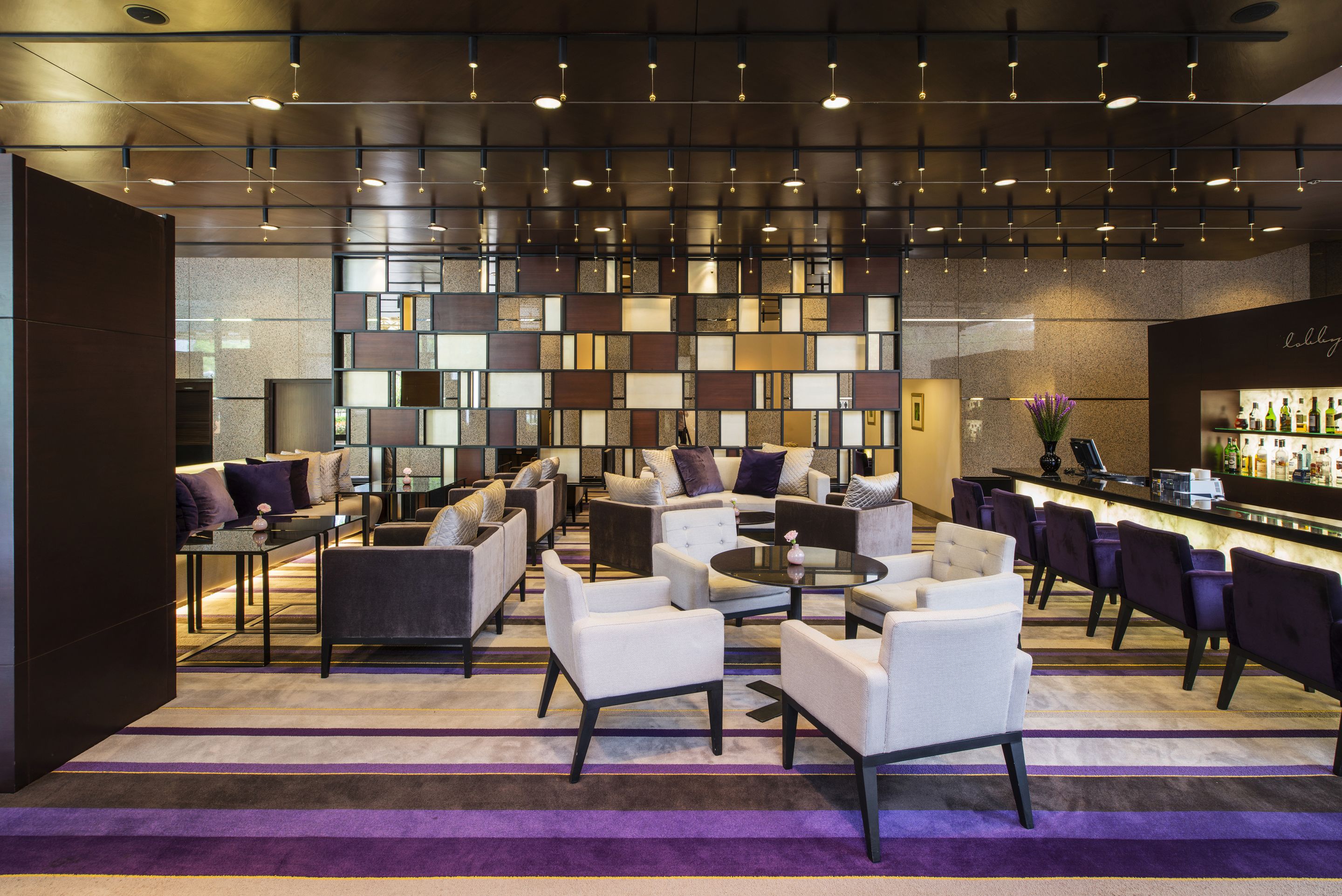 A modern lounge area with sofas and armchairs, a bar, and a patterned wall.