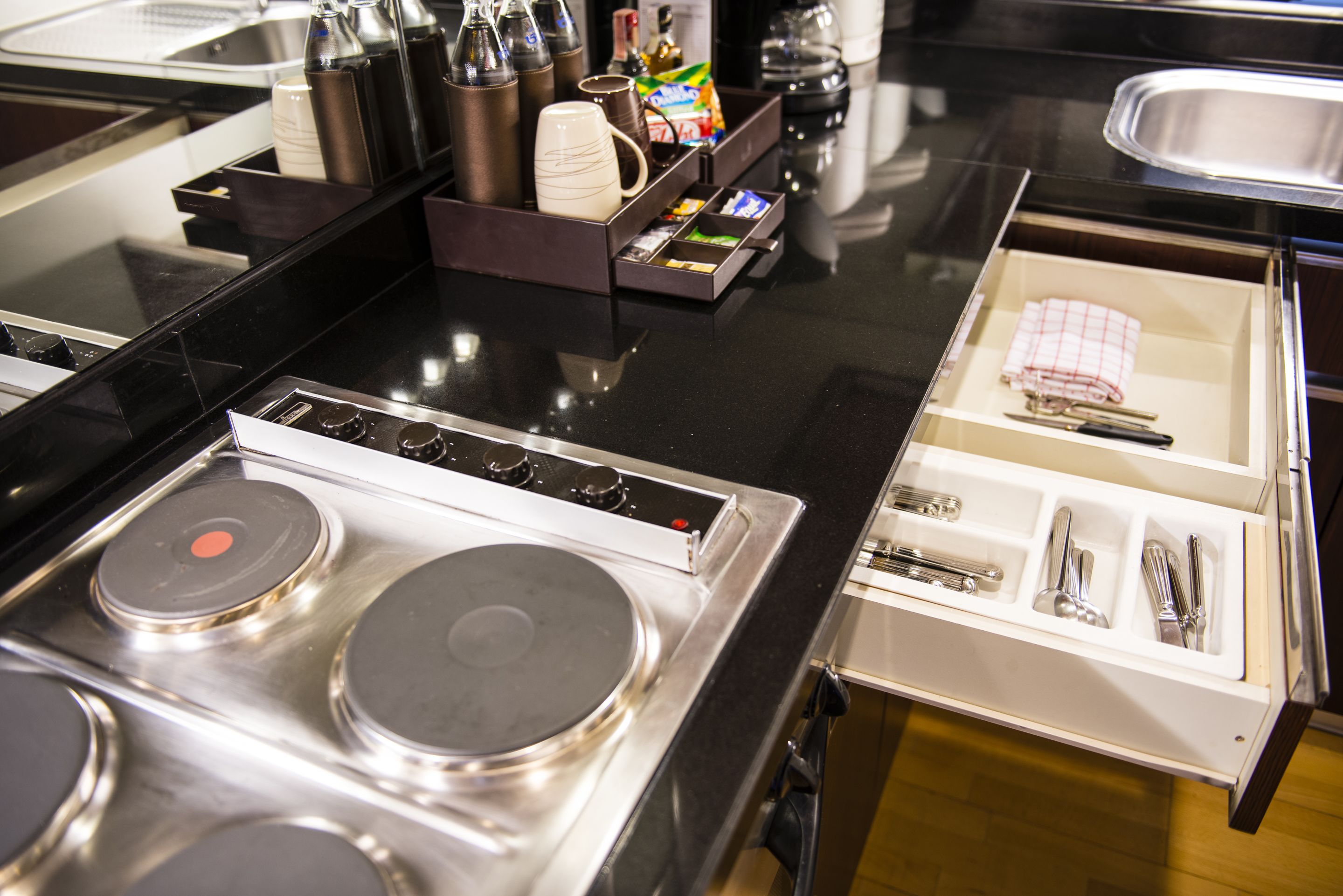 A kitchen area with a stove, a coffee machine, and a drawer with utensils.