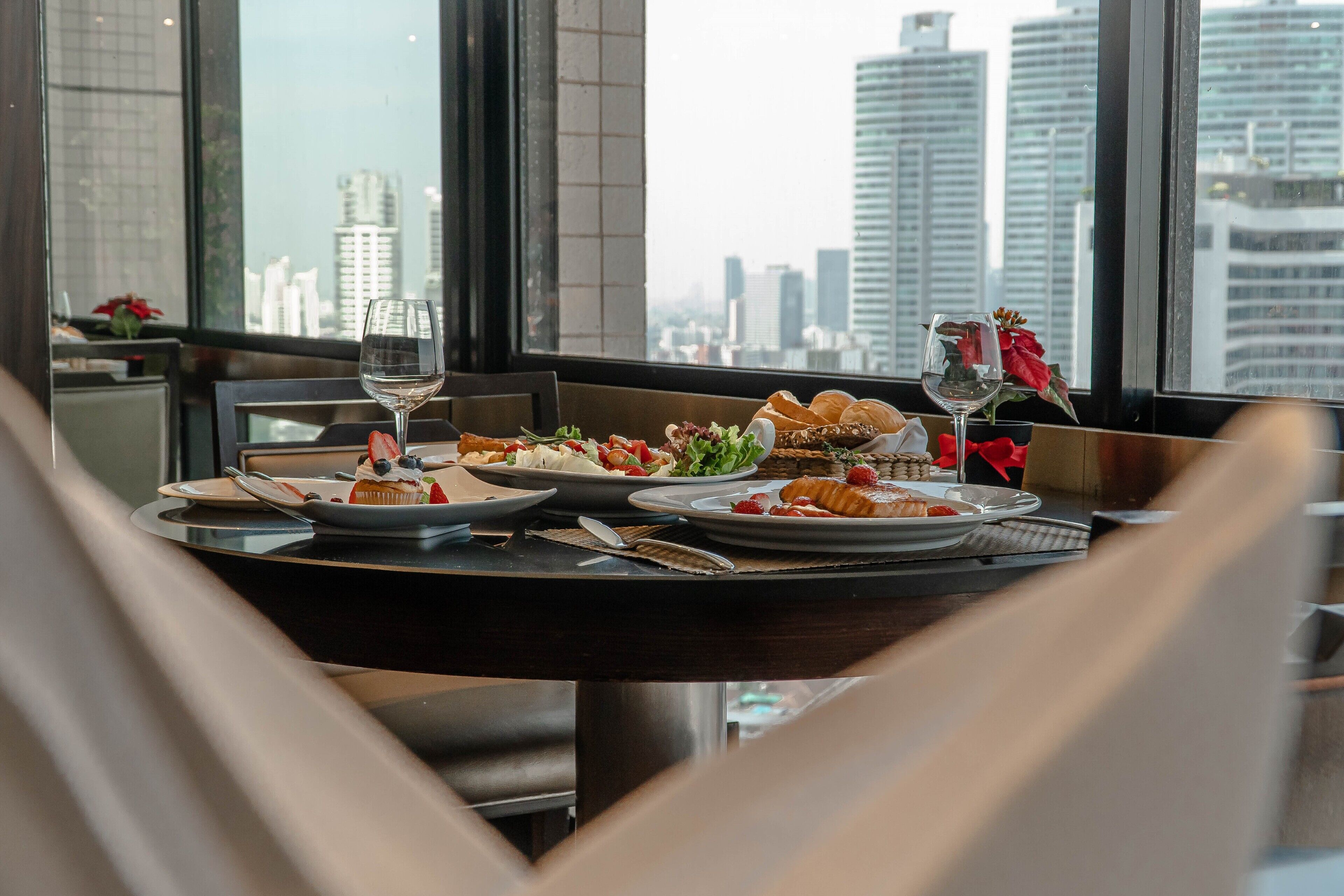 A dining table with plates of food and wine glasses, set against a city view.