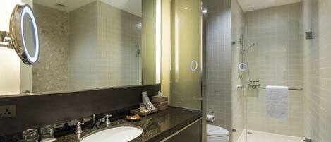 Un baño moderno con encimera de granito, lavamanos blanco, un espejo grande y zona de ducha con paredes de vidrio.
