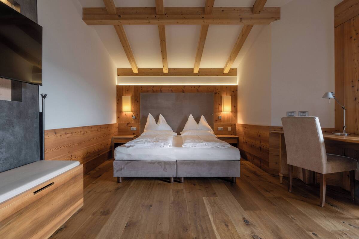 A modern bedroom with a wooden ceiling, a bed with a headboard, bedside tables, a desk, and a chair.