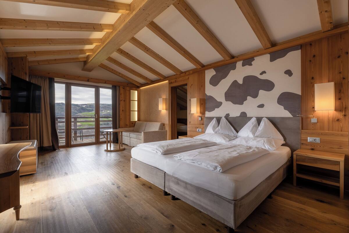 A bedroom with a large bed, wooden beams, a cow print wall, and a view of the outdoors.