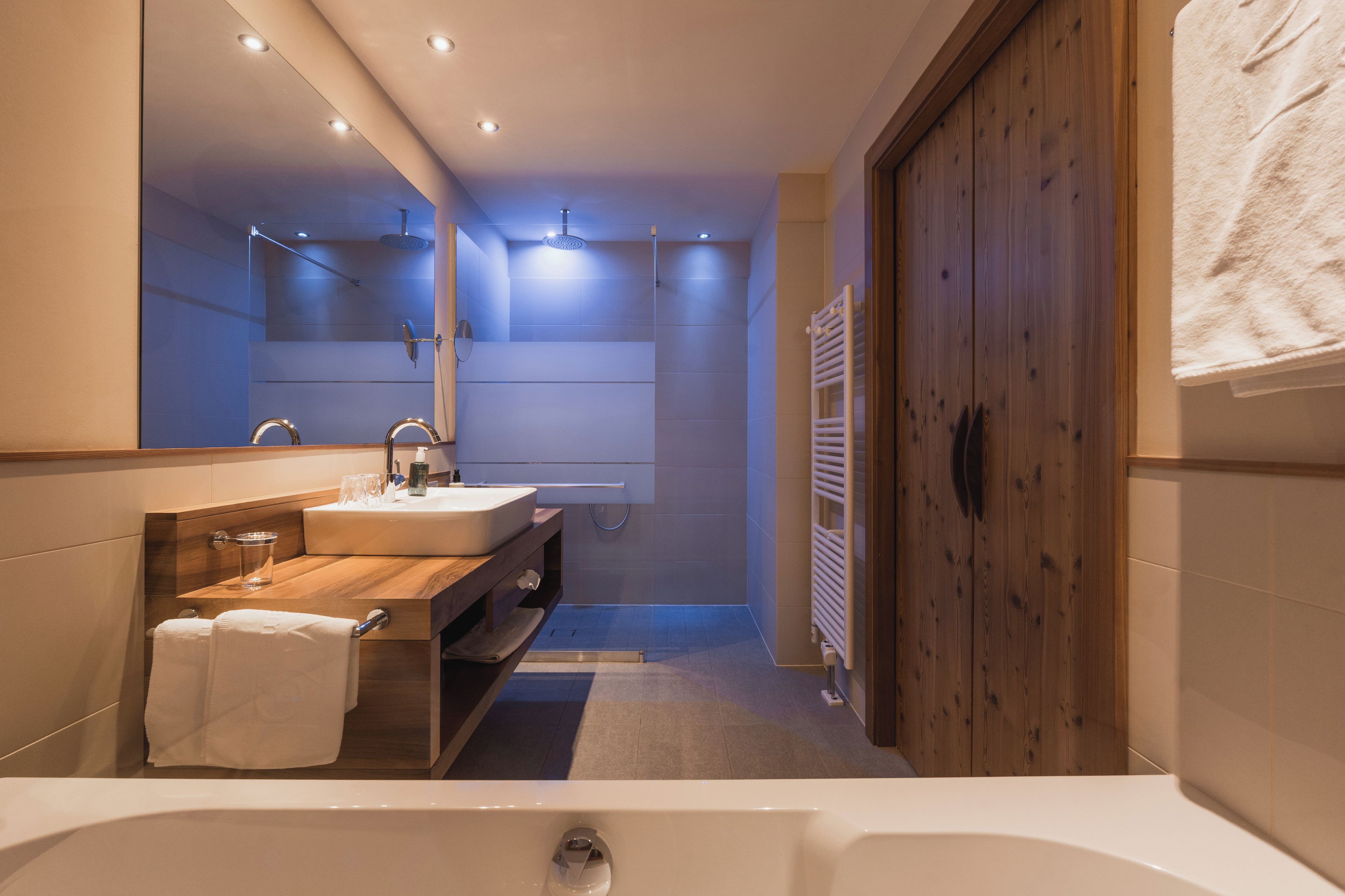 A modern bathroom with a large bathtub, a wooden vanity, a mirror, and a towel rack.