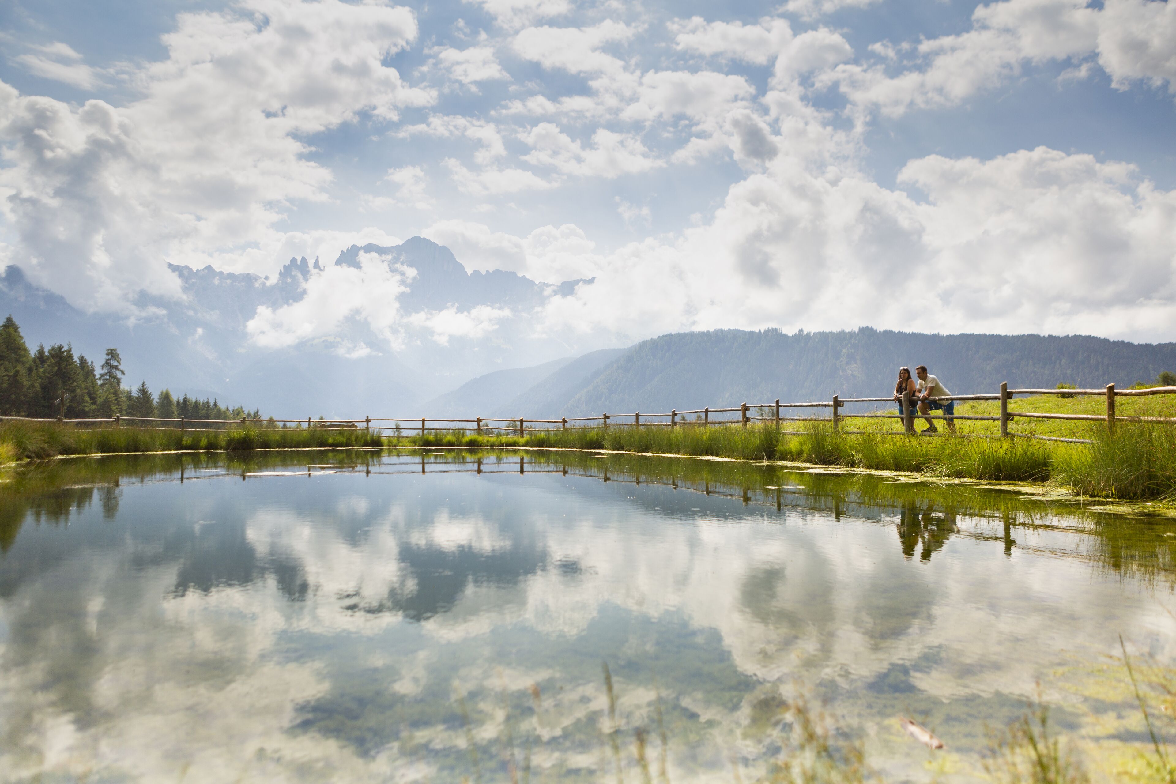 Escena serena junto al lago, con una valla de madera y una persona sentada cerca del agua.