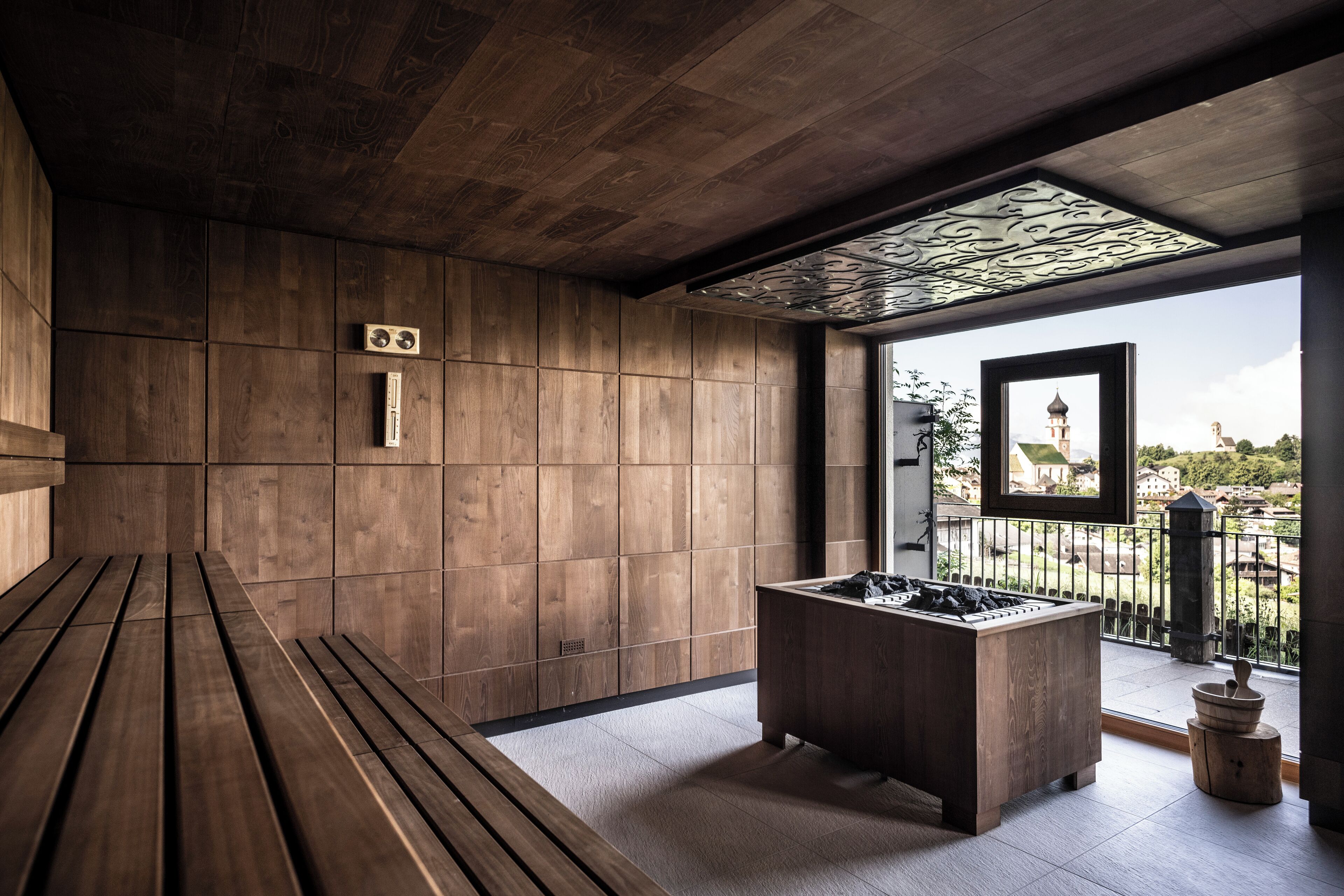 Interior de madera con un banco, estufa empotrada y vista a una torre a través de una ventana.