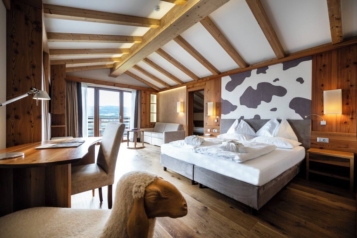 A bedroom with a large bed, a desk, and a chair. There is a view of the outdoors through a window.