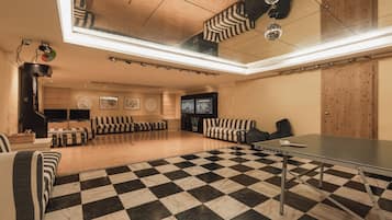 Una habitación amplia con piso de tablones de ajedrez, una mesa de billar, sofás a rayas y un televisor.