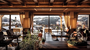 Un restaurante acogedor con vigas de madera y amplios ventanales que ofrecen vistas a montañas nevadas y una iglesia.