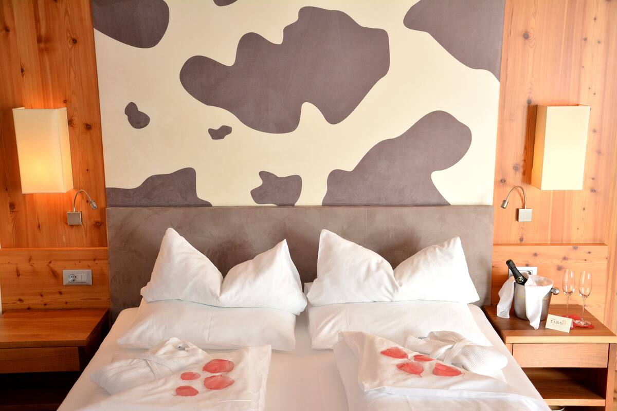 A hotel room with a large bed, two bedside tables, a wooden headboard, and a wall with a cow print design.