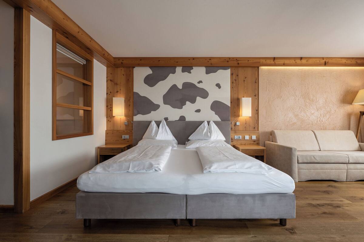 A modern hotel room with a large bed, wooden headboard, and a sofa.