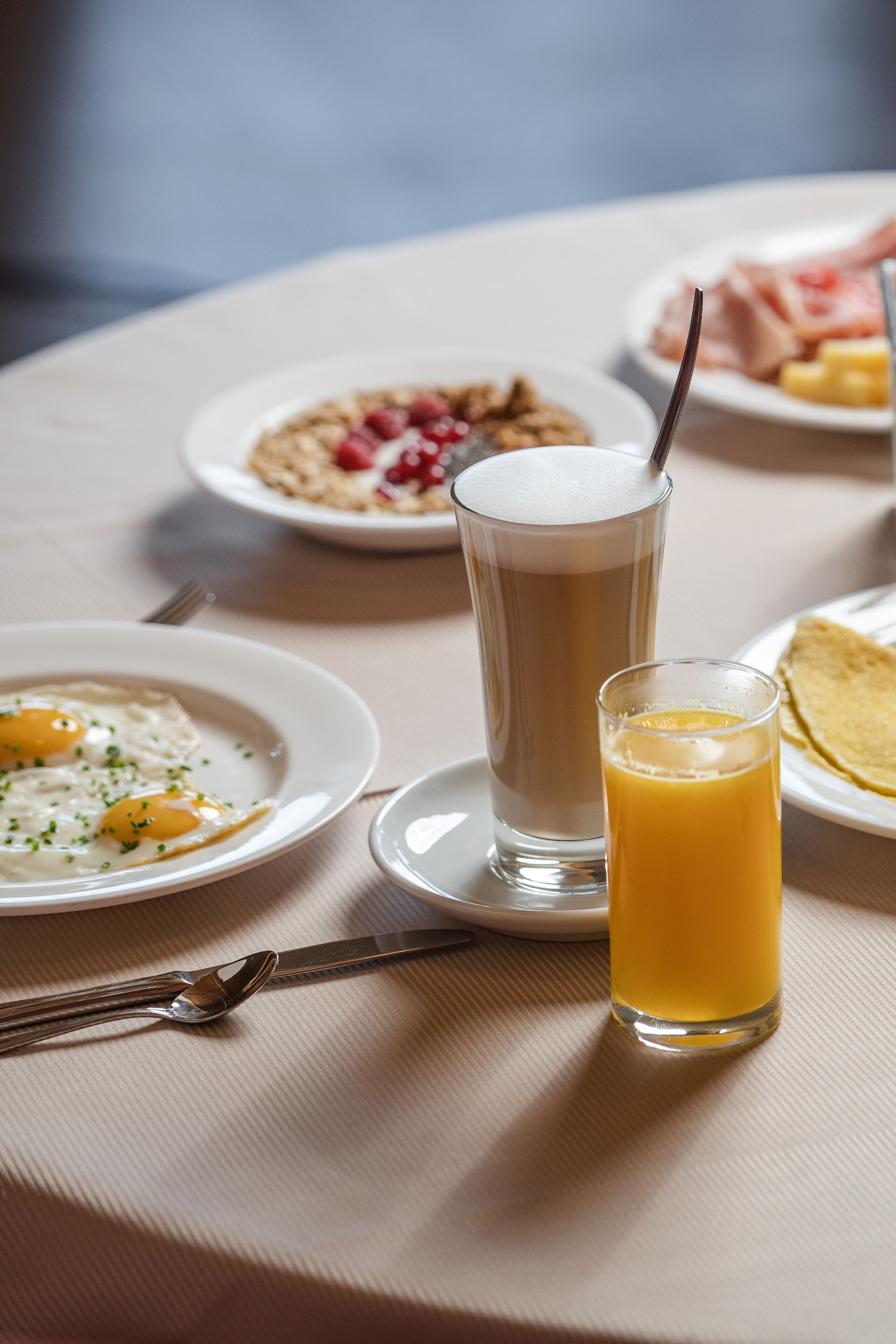A breakfast setting with plates of food, a tall glass of coffee, and a glass of orange juice on a table.