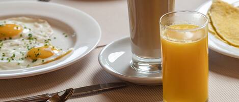 A breakfast setting with plates of food, a tall glass of coffee, and a glass of orange juice on a table.