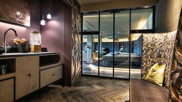 A modern bathroom with a wooden vanity, a glass shower enclosure, and a view into the bedroom area.