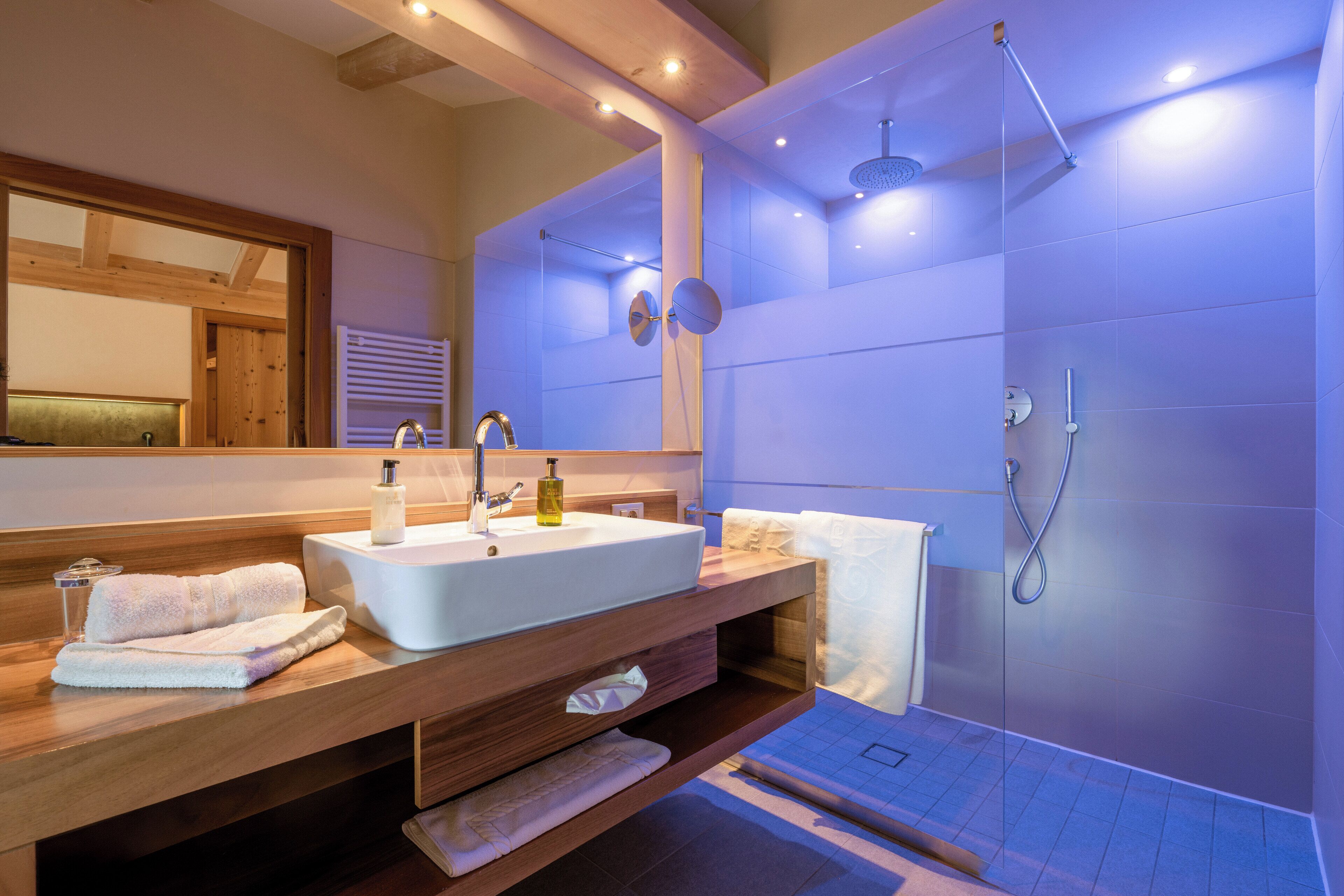 A modern bathroom with a wooden vanity, a large mirror, a white sink, and a glass shower enclosure.
