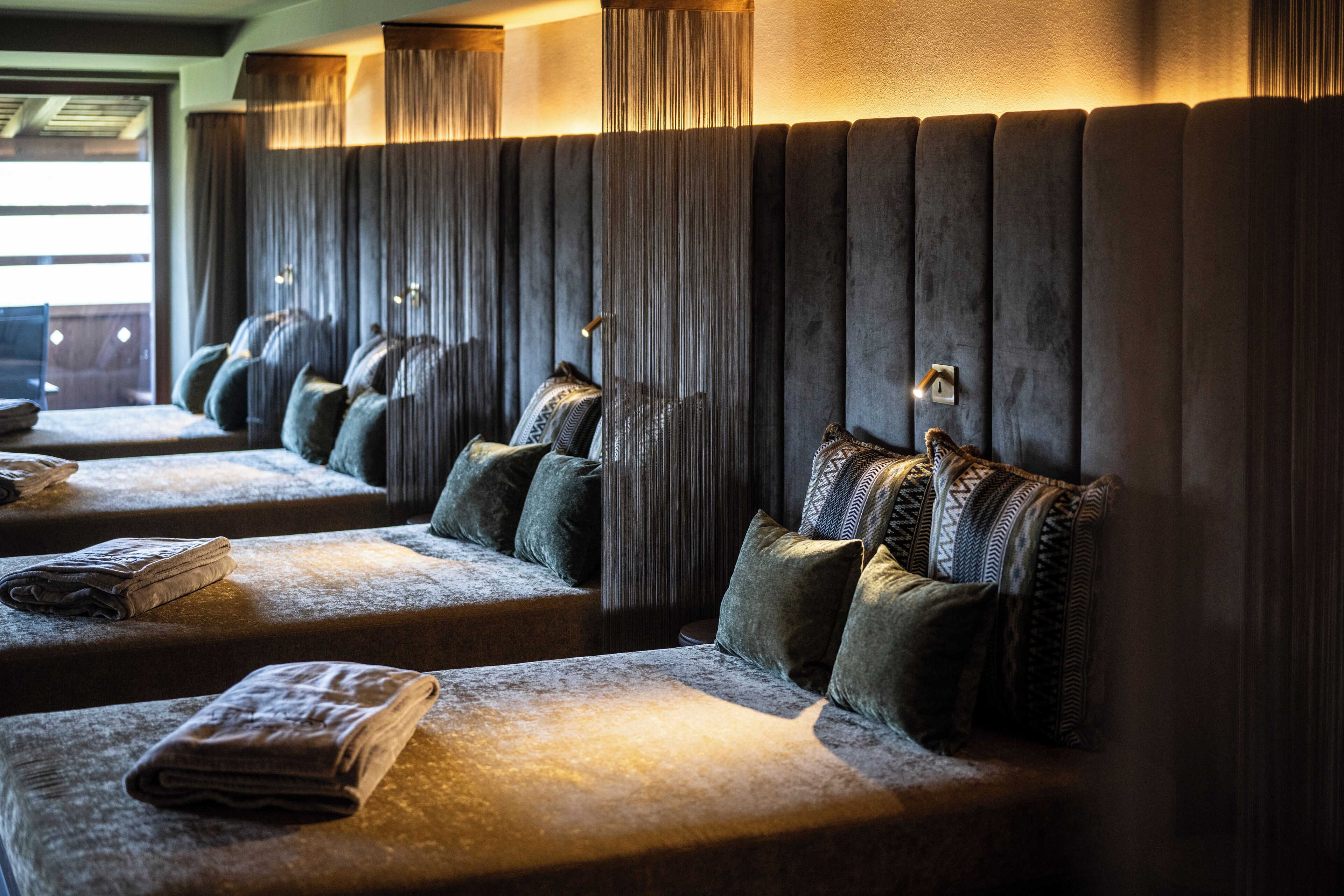 A row of dark-colored, plush headboards with vertical slats and a series of beds with folded towels and pillows.