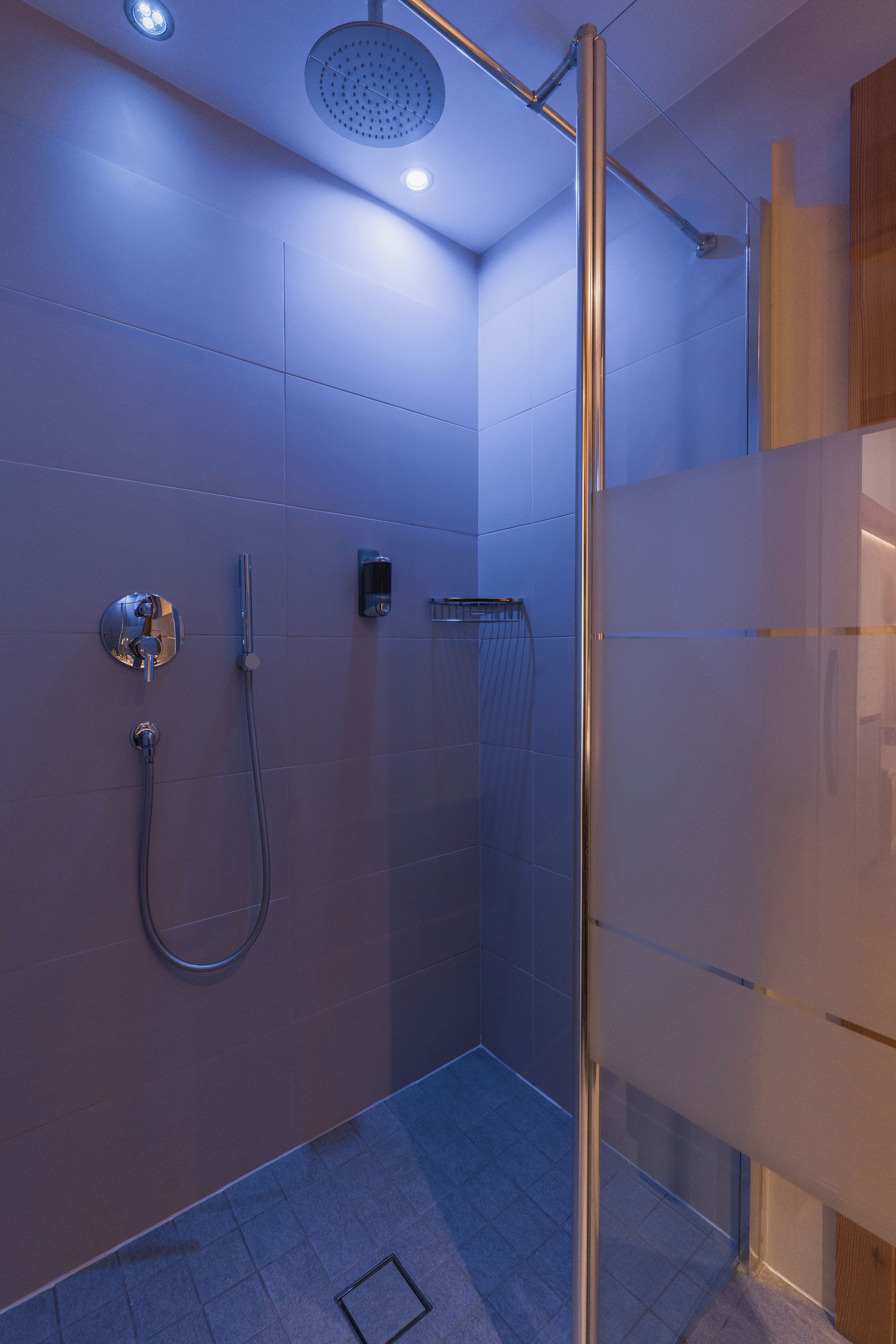 Un área de ducha moderna con mampara de vidrio, ducha de mano, grifo de pared y desagüe en el suelo.