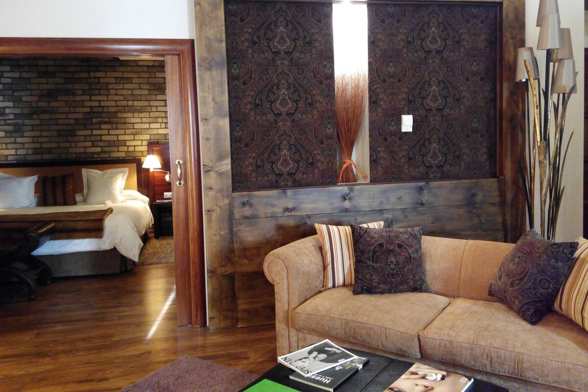 A room with a wooden floor, a sofa with patterned cushions, a brick wall, and a bed with white bedding.