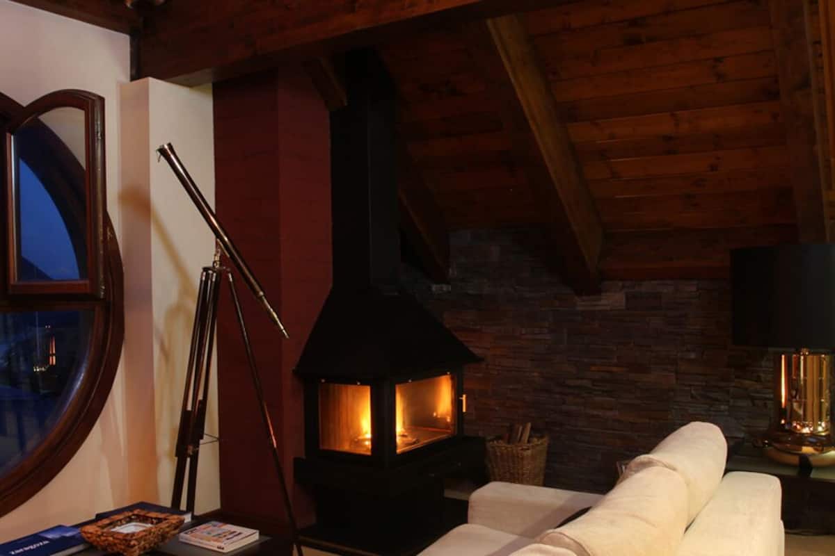 A cozy room with a fireplace, a round window, and a view of mountains.