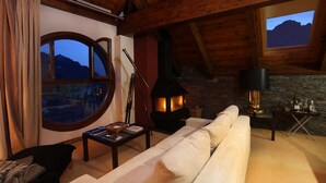 A cozy living room with a stone fireplace, a large round window, and a view of mountains.