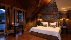 A bedroom with a wooden ceiling, a large bed, two bedside tables with lamps, and a view of the outside.