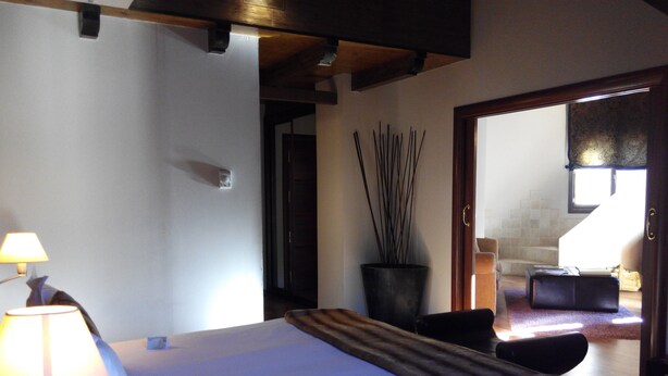 Un dormitorio con cama, mesita de noche, lámpara, planta en maceta y vista al baño.