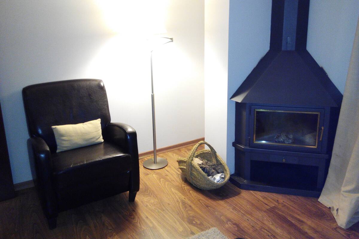 A living room with a black leather chair, a floor lamp, a woven basket, and a wood-burning stove.