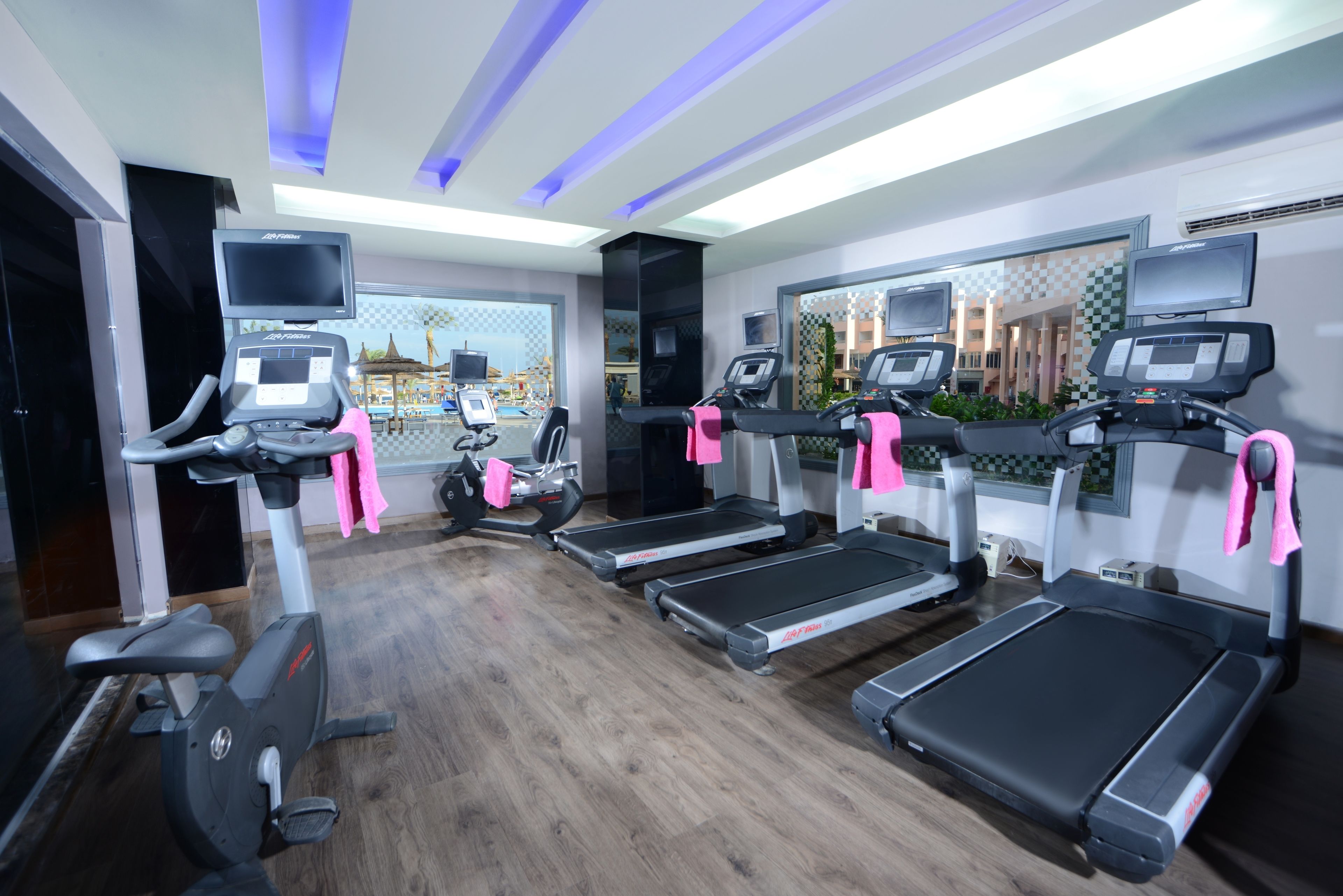 Un gimnasio con cintas de correr, elípticas y bicicletas estáticas, equipado con monitores de frecuencia cardíaca y un espejo grande.