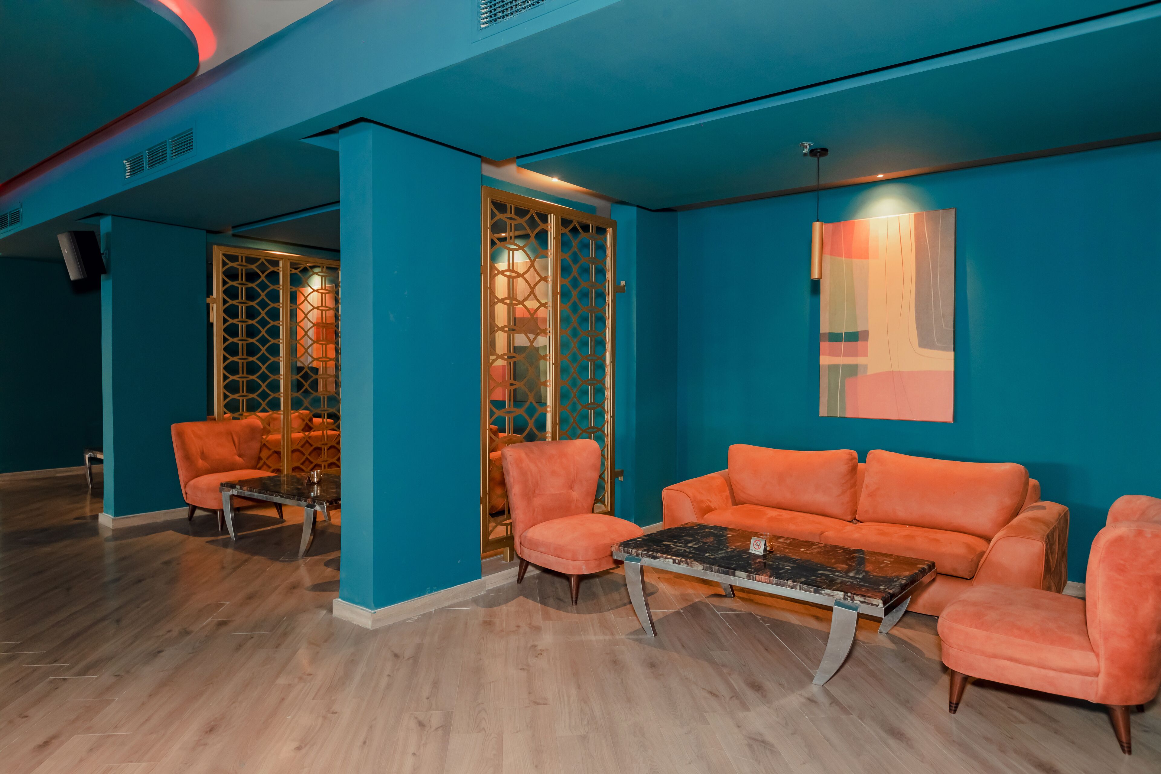 A room with teal walls, orange sofas, and a wooden floor.